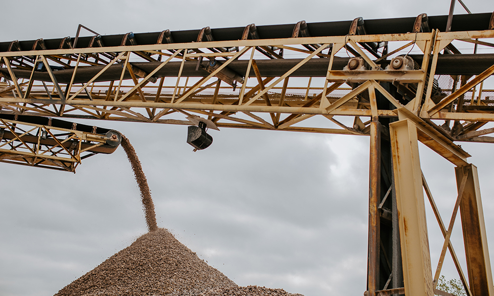 A conveyer belt drops crushed rock into a pyramid shaped pile